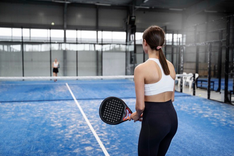 Female padel player ready to serve on indoor court Woman holding a padel racket, preparing to serve on a blue indoor court