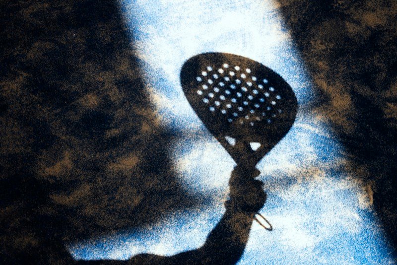 Shadow of padel racket on court surface Shadow of a hand holding a padel racket on a textured blue court