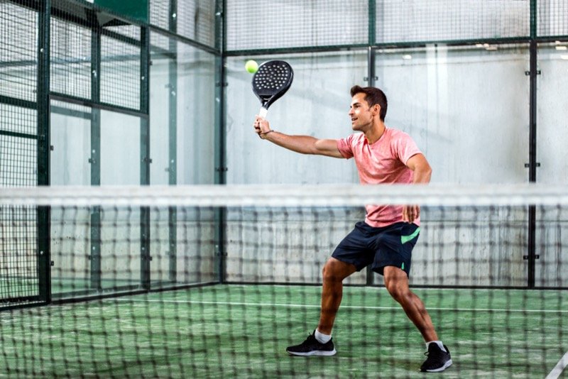 Padel player hitting a shot on indoor court Man swinging a padel racket, returning the ball on an indoor green court