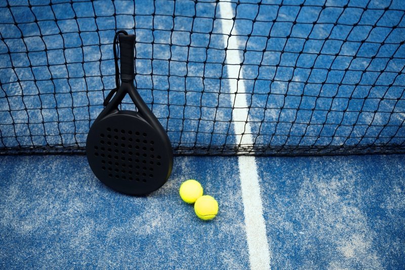 Padel racket and tennis balls near the net on the court