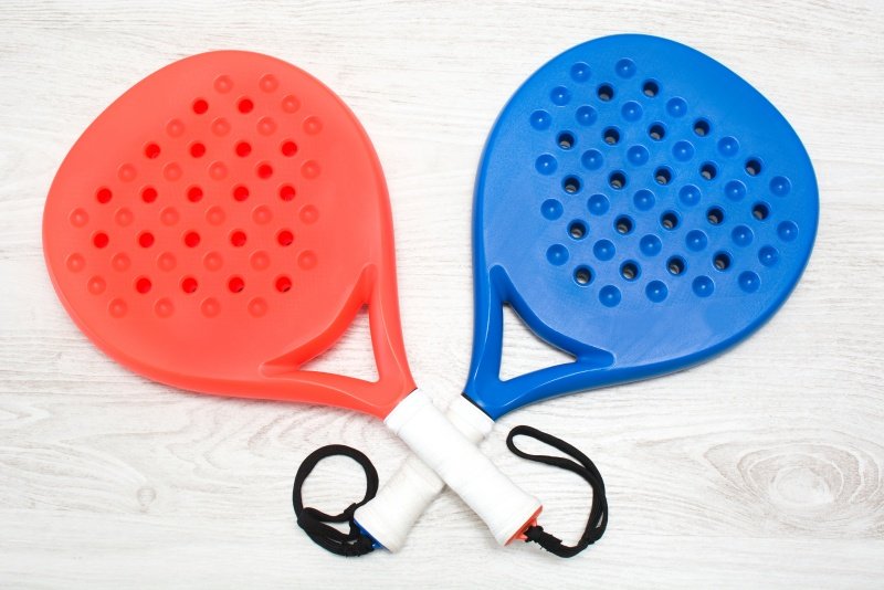 Red and blue padel rackets on wooden surface Two colorful padel rackets, red and blue, with handles wrapped