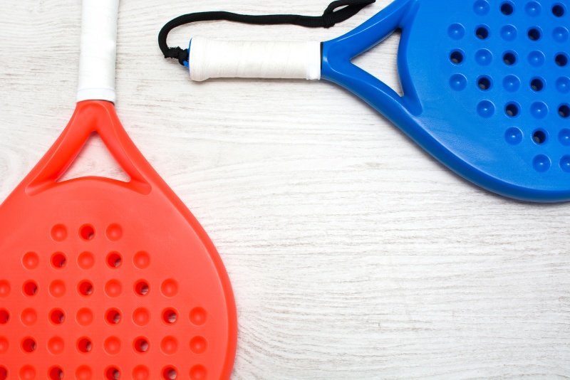 Red and blue perforated padel rackets Red and blue padel rackets with perforated surfaces on white table