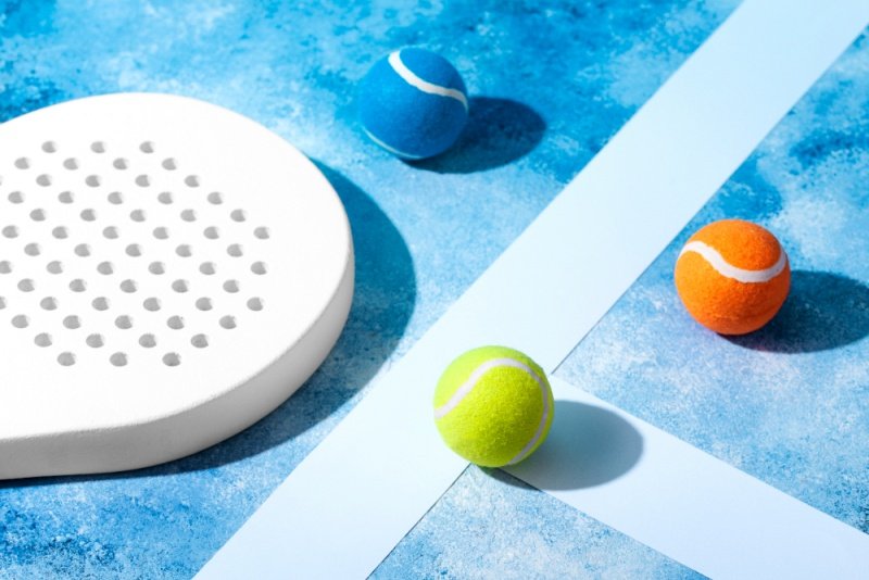 White padel racket and tennis balls White padel racket with colorful tennis balls on blue surface