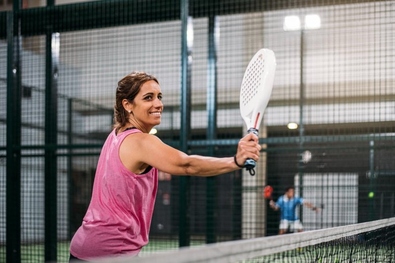 female-padel-backhand Female padel player hitting backhand, indoor court, smiling, pink top