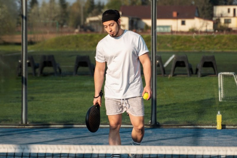 padel-player-ball-racket-court man walking on padel court holding racket and ball