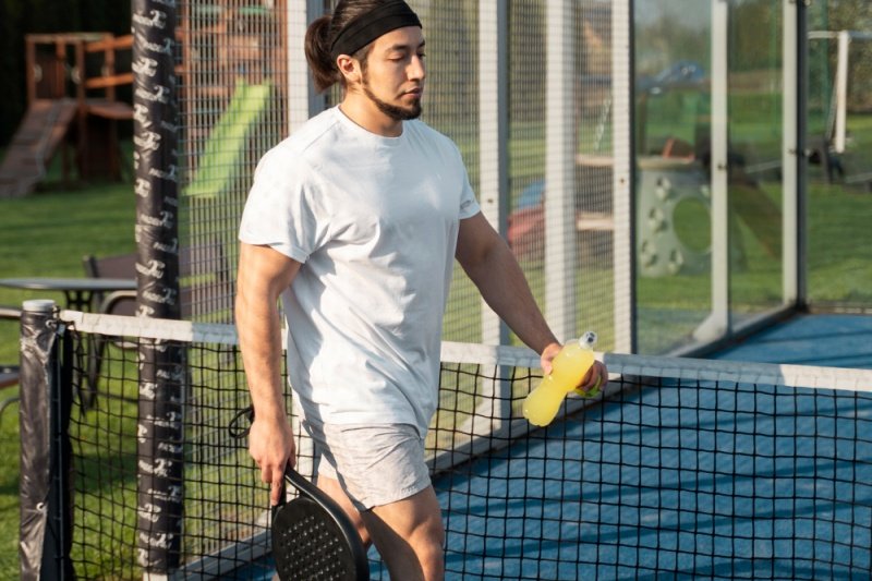 padel-player-refreshment-court man walking with padel racket and drink