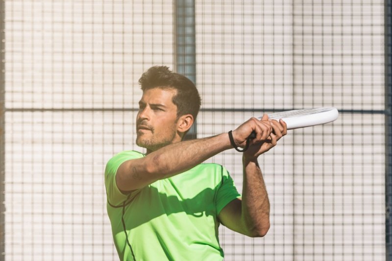 padel-player-swing Padel player hitting ball with racket, green shirt, action shot