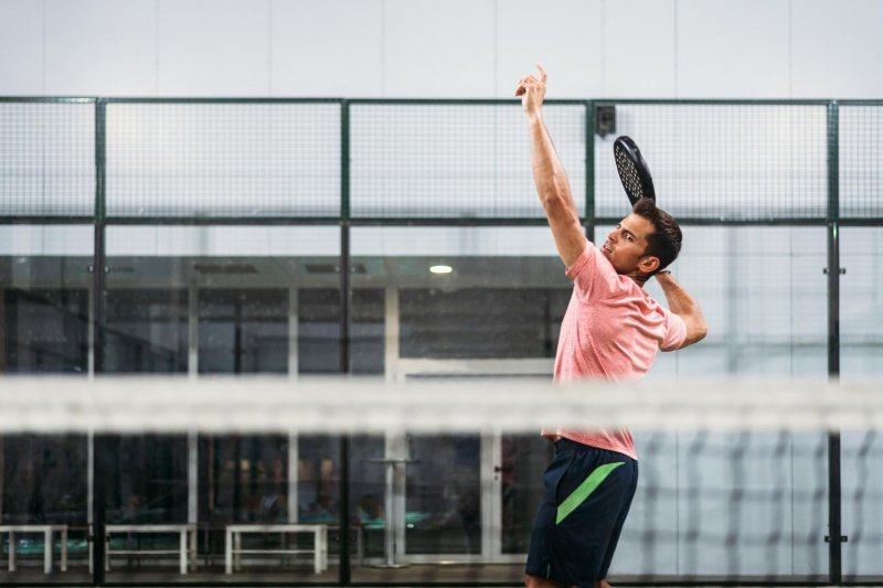 padel-serve-action Padel player serving, indoor court, red shirt