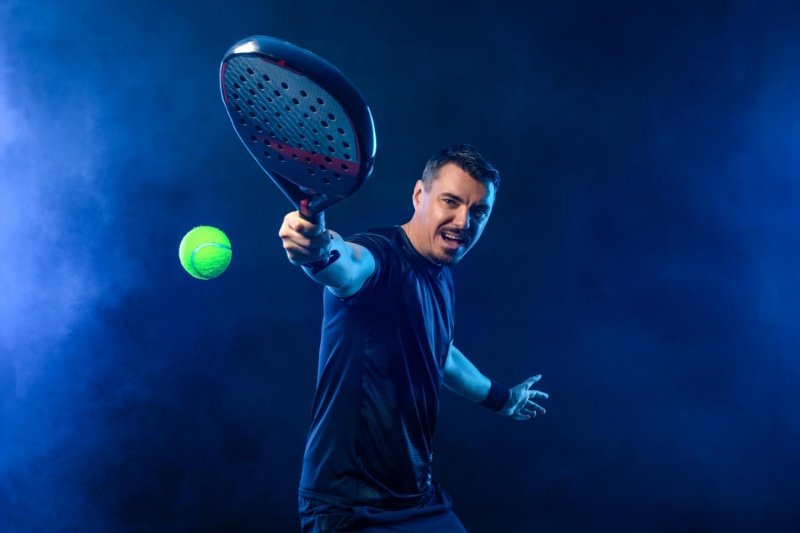 Padel player in action hitting ball with racket in studio