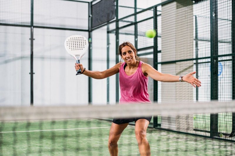 Excited woman playing padel Smiling female padel player hitting the ball