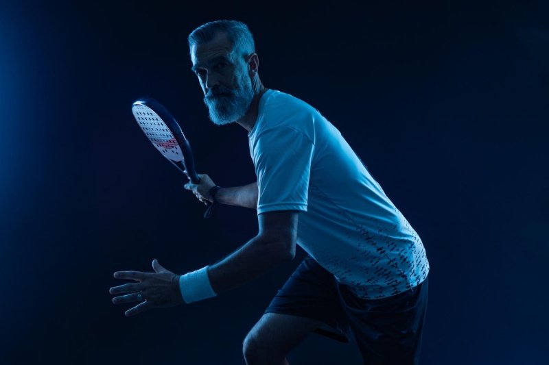 Focused padel athlete ready to play Senior padel player in action under blue lighting
