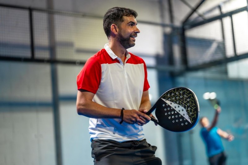 Happy padel player ready to play Smiling padel player in white and red shirt holding racket on indoor court