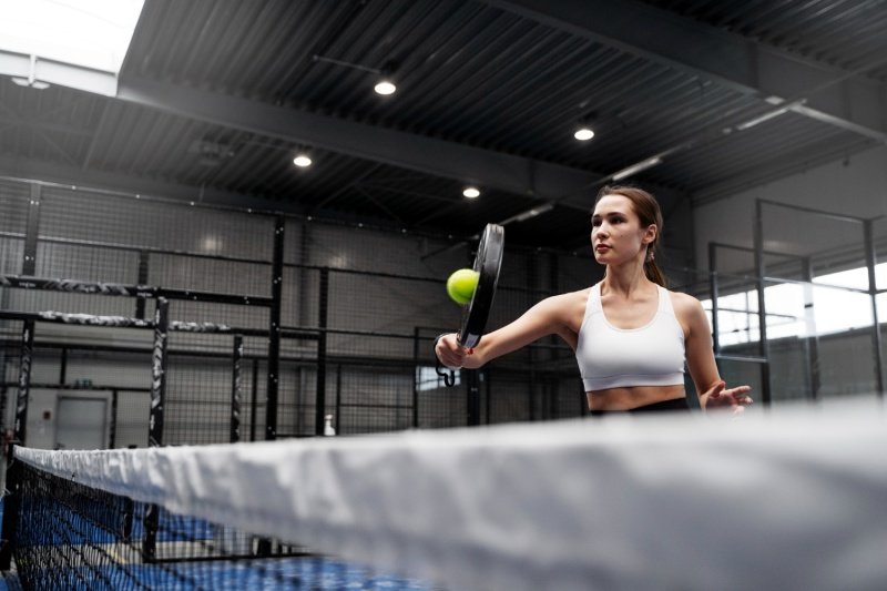 Indoor Padel Action Shot Female padel player hitting ball indoors near net
