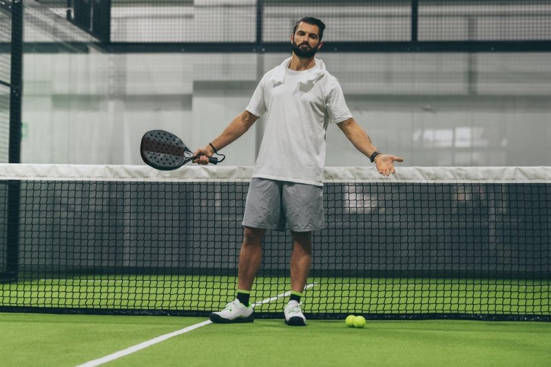 Indoor Padel Court Pose Padel player standing on green indoor court with racket and balls