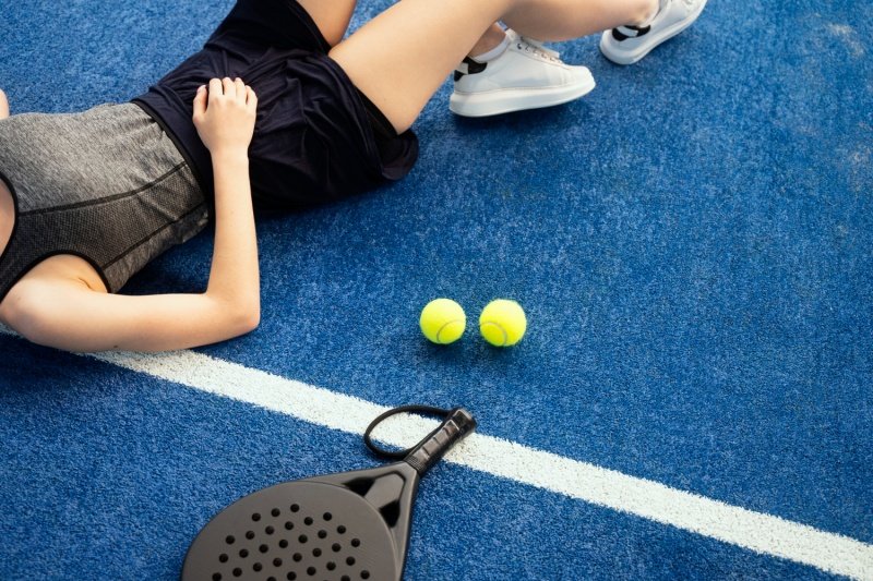 Padel Court Rest Moment Female padel player resting on blue court beside racket and balls
