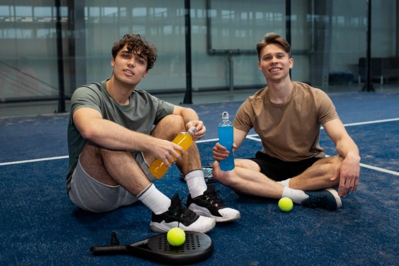 Two padel players resting with drinks on court