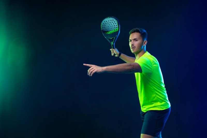Male padel player in neon shirt ready to serve