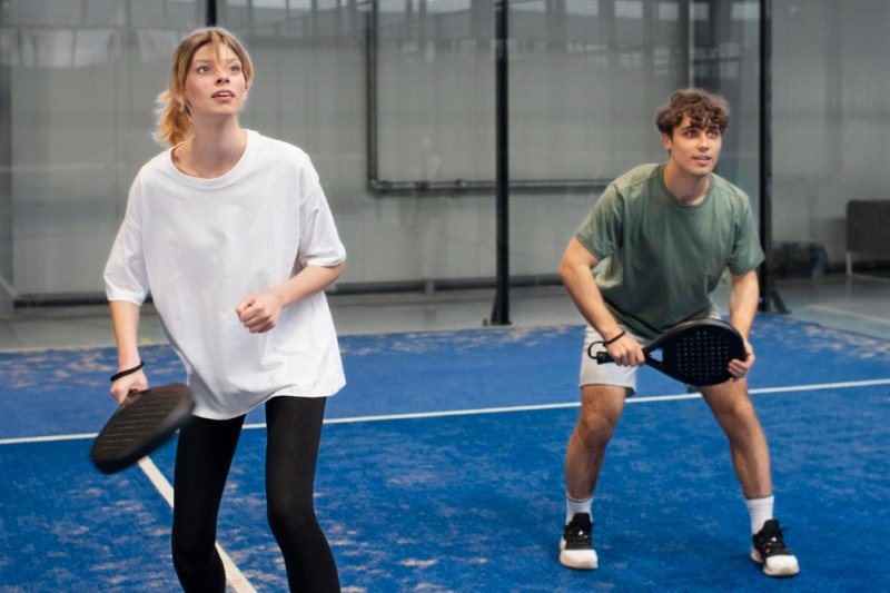 Male and female padel players in ready position on a blue court