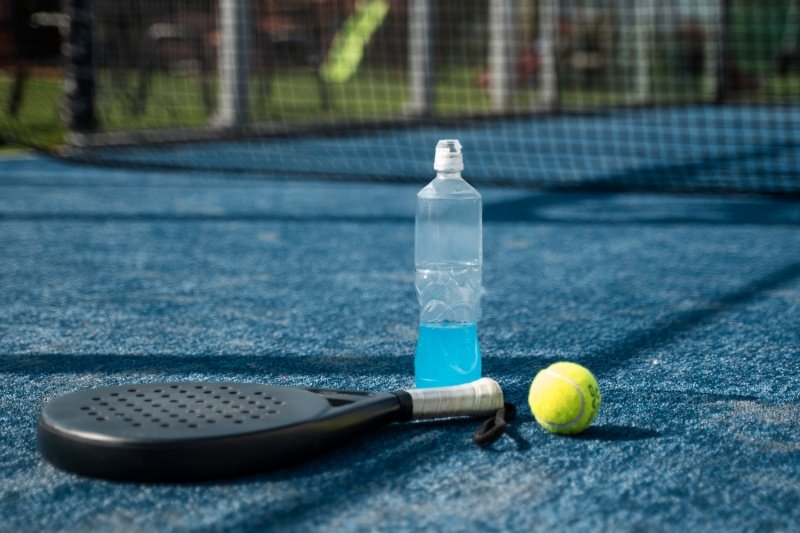Padel equipment on court Padel racket, ball, and sports drink on blue court