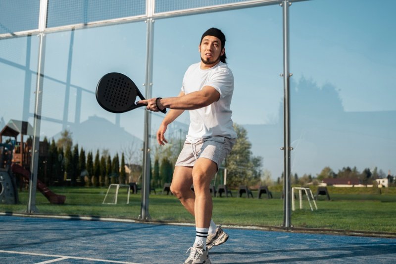 Padel player in white outfit swinging racket on outdoor glass court