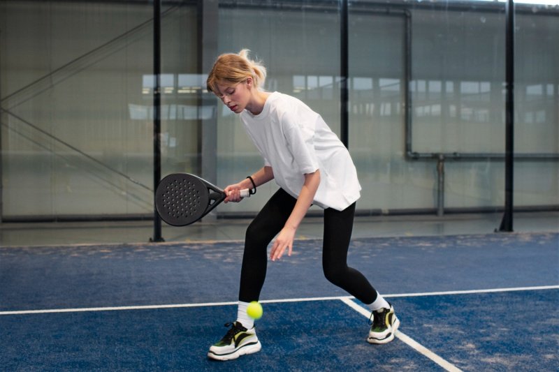 Female padel player preparing to hit a ball with a black racket on a blue court
