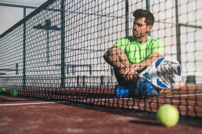 Padel player resting on court Padel player sitting by the net with racket