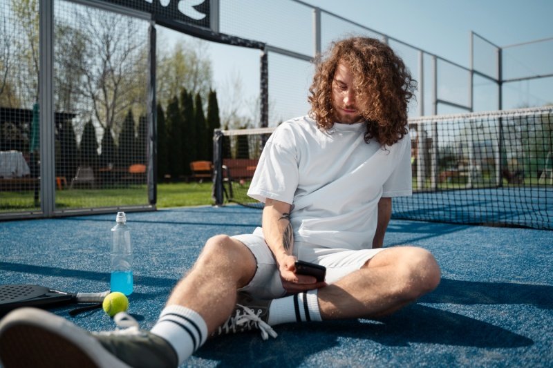 Padel player taking a break Padel player resting on court while checking phone