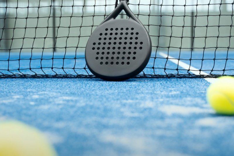 Padel racket and balls Black padel racket leaning against net on blue court with yellow balls
