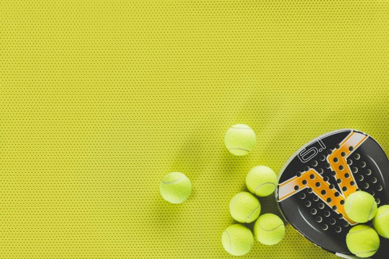 Padel racket and balls Black and yellow padel racket with multiple balls on bright yellow surface