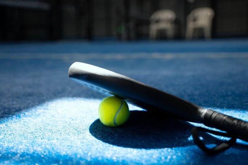 Padel racket on ball Black padel racket resting on yellow ball on blue court