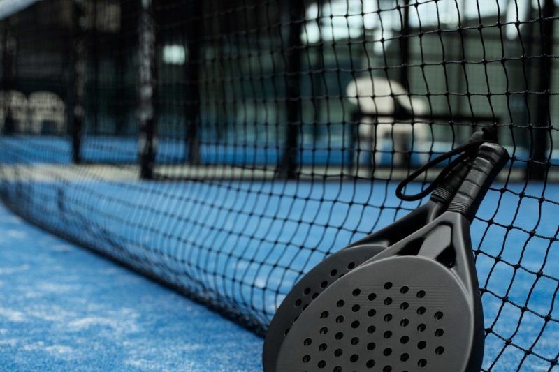 Padel rackets on court Black padel rackets resting against net on blue court