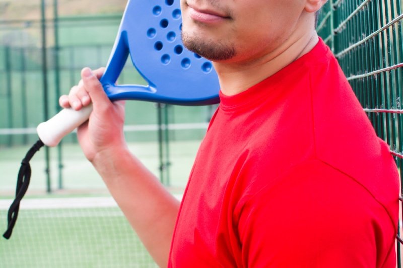Relaxed padel player on court Padel player in red shirt holding blue racket by the fence