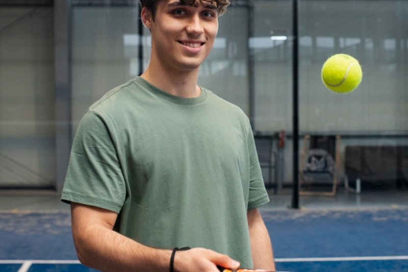 Padel player smiling with ball mid-air