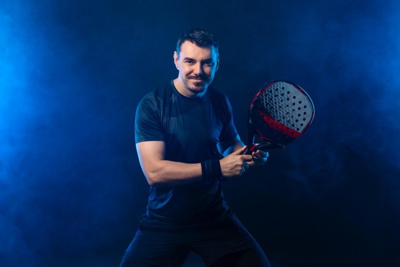 Male padel player posing with black and red racket in studio