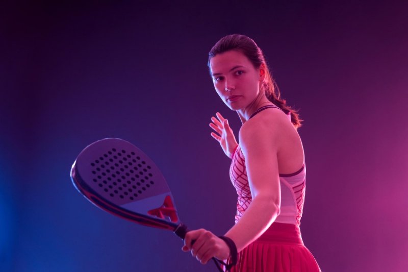 Female padel player posing with racket under pink and blue lights