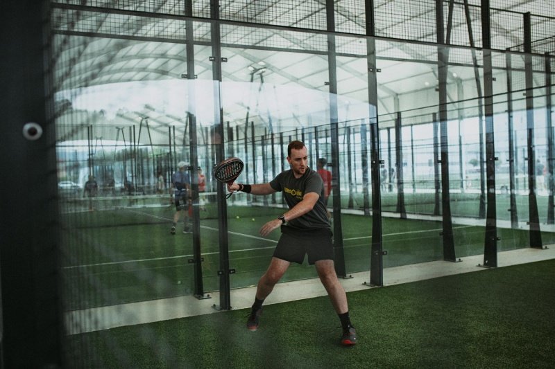 Indoor Green Padel Court padel player preparing backhand shot on green indoor court with glass walls