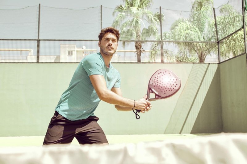 Young padel player with red paddle on sunny outdoor court