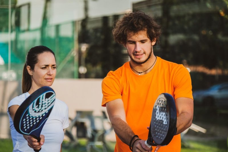 Padel instructor in orange shirt guiding female player outdoors