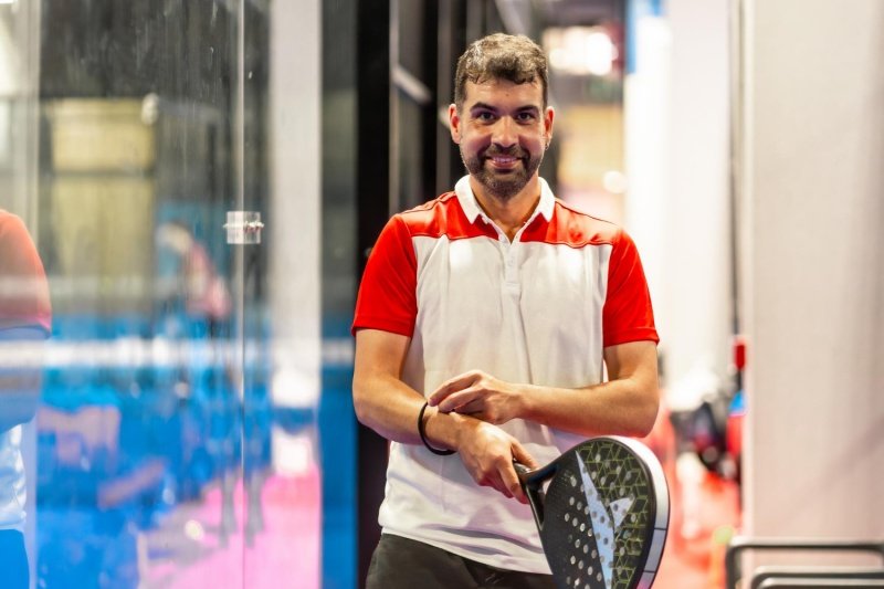 Padel Player Portrait padel player smiling and holding racket beside indoor court glass wall
