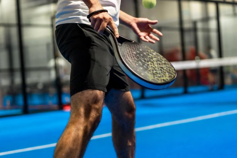Padel Serve Action close-up of padel player serving ball on blue indoor court