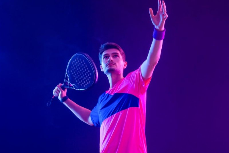 Padel player in pink shirt preparing to serve under dramatic lighting
