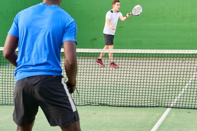 padel-doubles-action Two players on a padel court, one in blue shirt and the other preparing to hit a ball