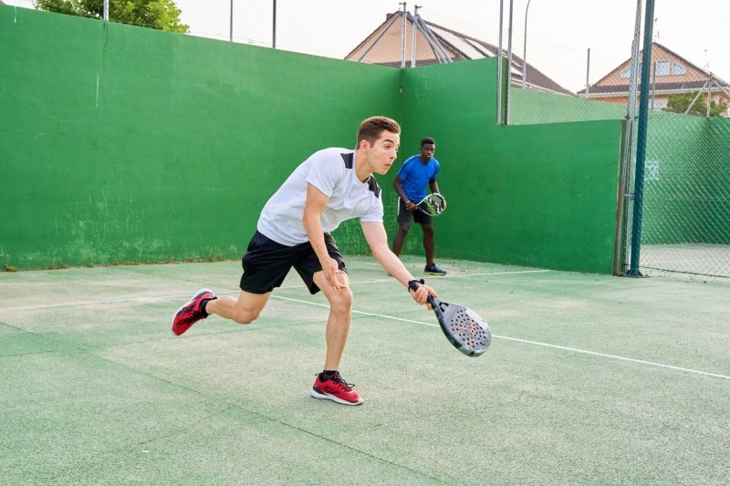 padel-doubles-movement Two players in action on a padel court, one in white shirt and the other in blue