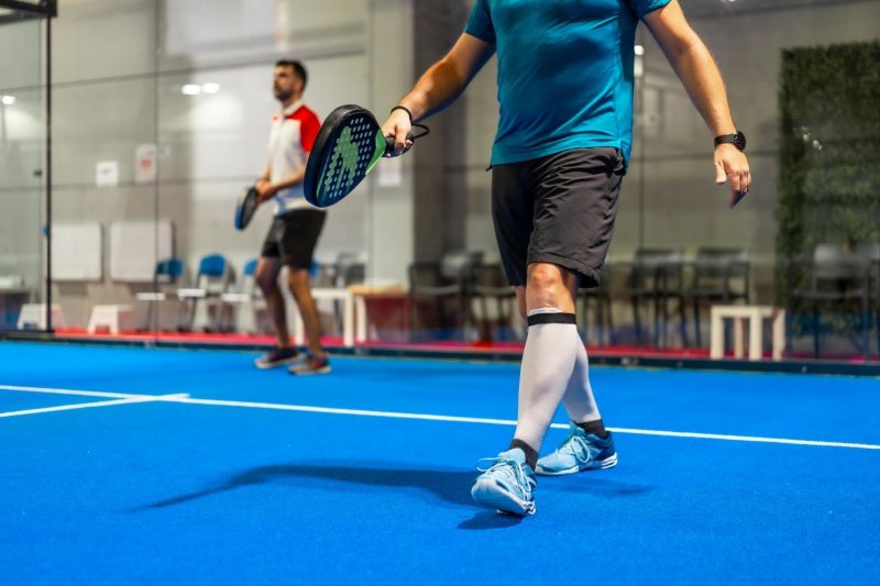 padel-indoor-play Two men playing padel on a blue indoor court