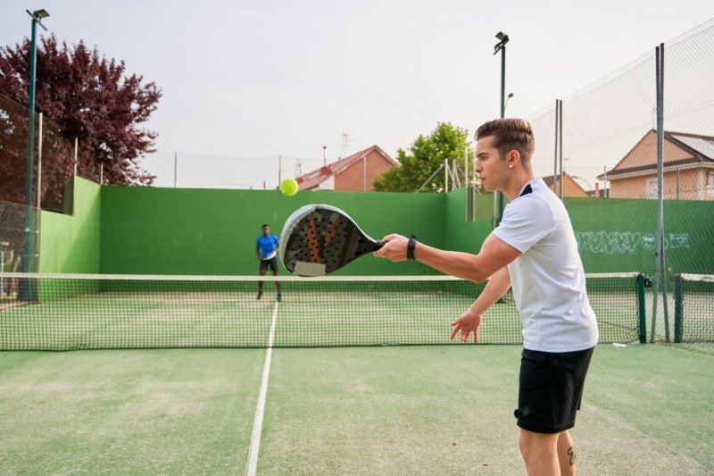 padel-match-action Player in white shirt hitting a padel ball with racket, opponent in blue shirt behind