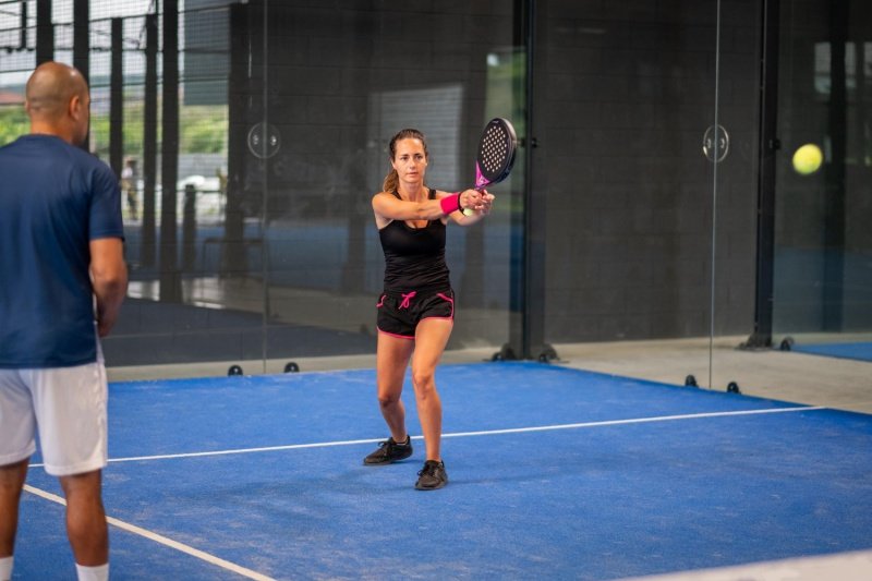 Padel Backhand Practice Focused female player prepares two-handed backhand shot during padel lesson