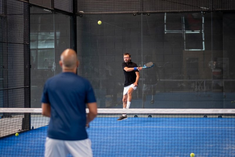 Padel Backhand Return Indoor padel player returns shot with backhand as opponent watches