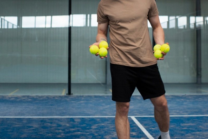 holding padel balls man holding multiple yellow padel balls on blue padel court
