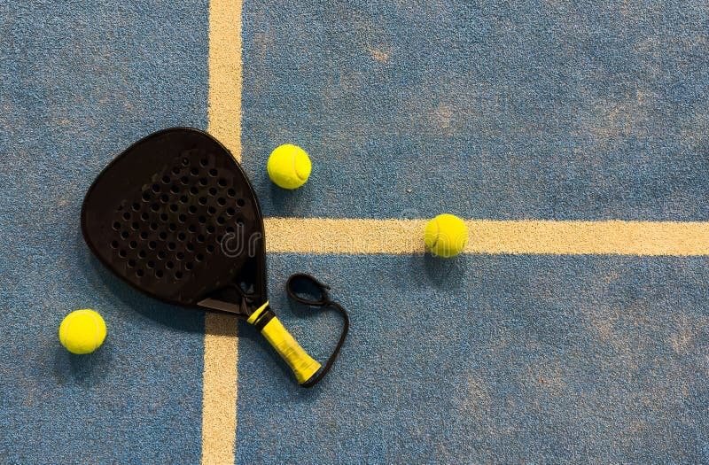 padel-racket-court-balls black padel racket with yellow grip and balls on blue court
